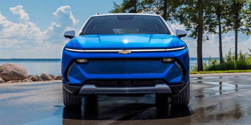 Front view of a blue Chevrolet Equinox EV parked on a wet road near a lake with trees in the background.