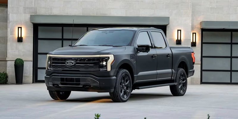 A matte black Ford F-150 Lightning pickup truck parked in a driveway in front of a modern house.