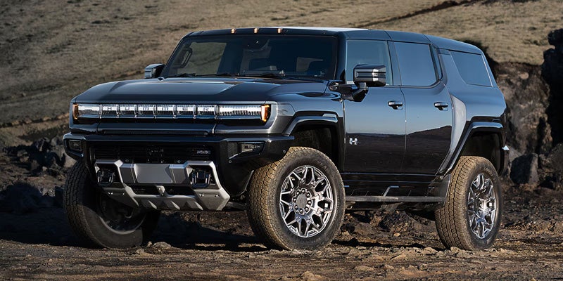 A dark grey GMC Hummer EV SUV parked on a rocky, dry terrain.