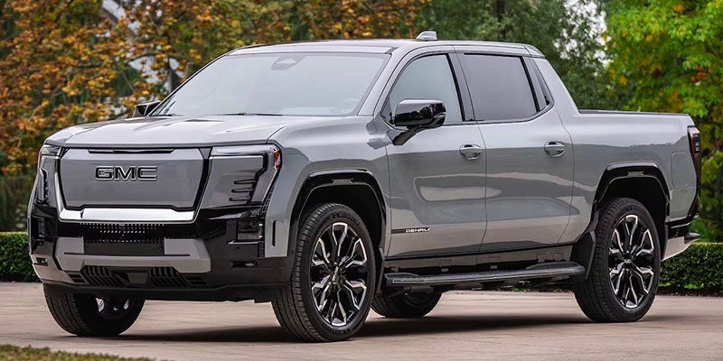 Front 3/4 view of a grey GMC Denali Electric Pickup Truck with multi-spoke wheels, parked outdoors on an overcast day.