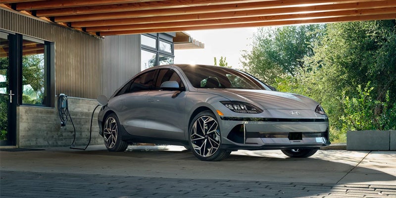 A silver-gray Hyundai IONIQ 6 electric car parked and charging under a modern carport with wood beams and metal siding.