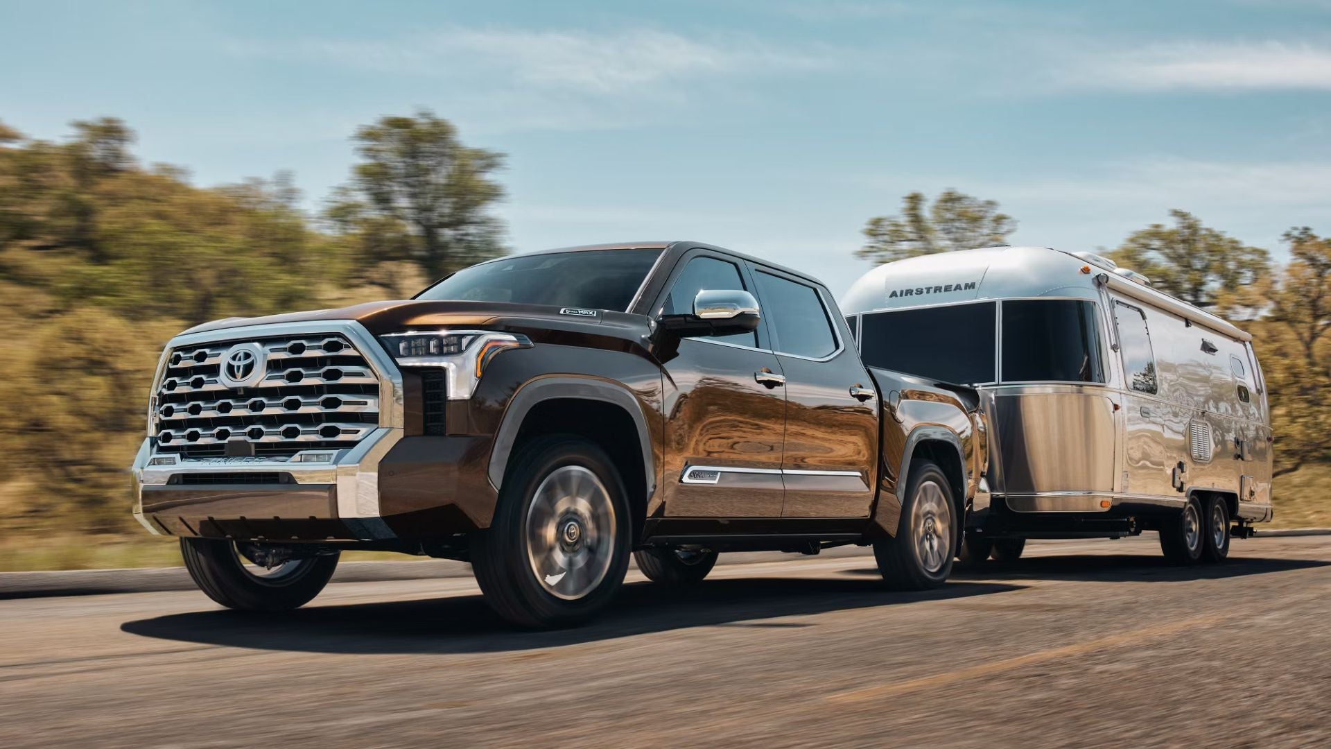 Brown Toyota Tundra pickup truck pulling a silver Airstream travel trailer on a road with blurred background.