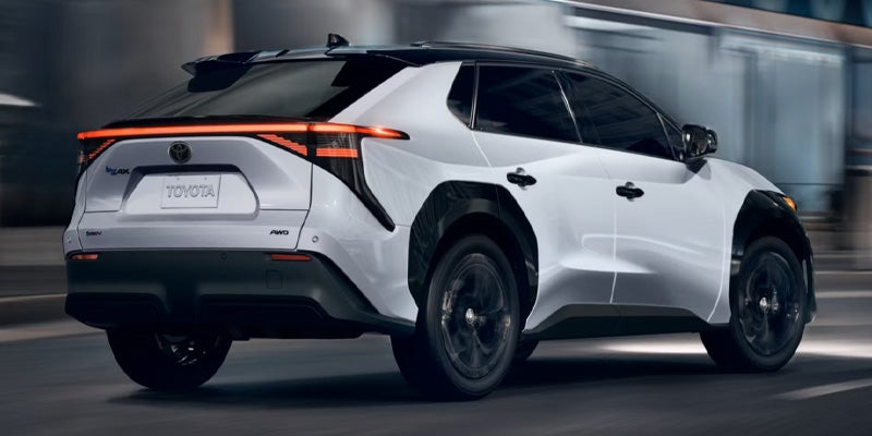 Rear three-quarter view of a white Toyota bZ4X electric SUV with black trim and partially illuminated taillights.