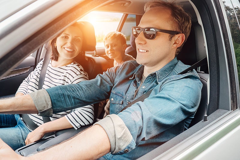 Happy family - father, mother, and child - smiling, buckled up in a car on a sunny day.