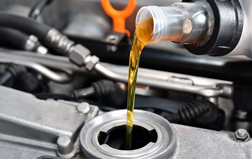 Golden motor oil pours from a clear plastic bottle into a car's engine.