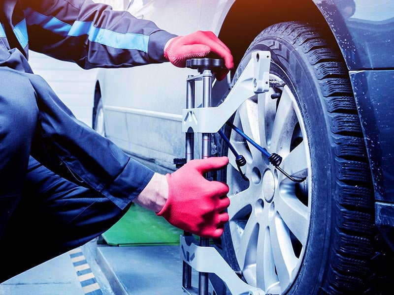 Mechanic in red gloves using a laser aligner on a car wheel, performing wheel alignment service.